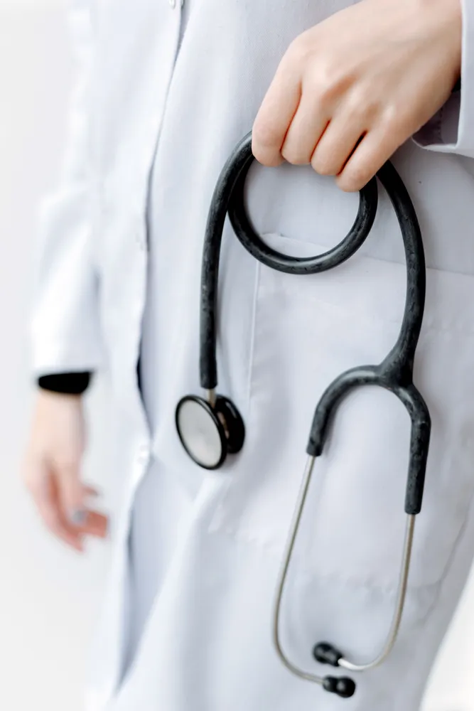 A clinician in a white coat with a stethoscope, face out of frame.